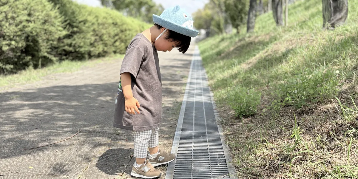木かげの散歩道で、みぞのふたをのぞきこむ子ども