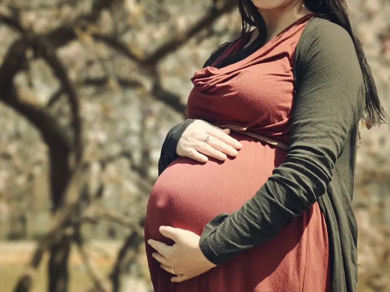 花の咲いた木の前で、服の上からおなかに手を当てる妊婦